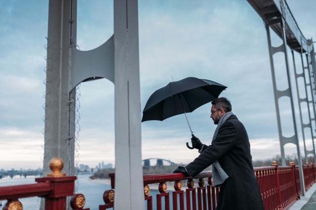handsome lonely man with umbrella standing on bridge