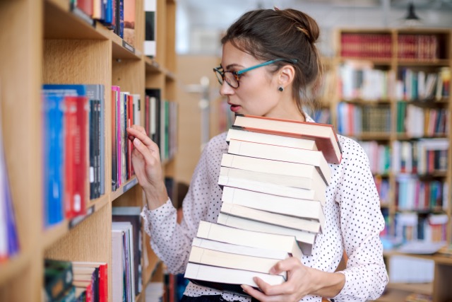 Young woman with a stack of books in library want more