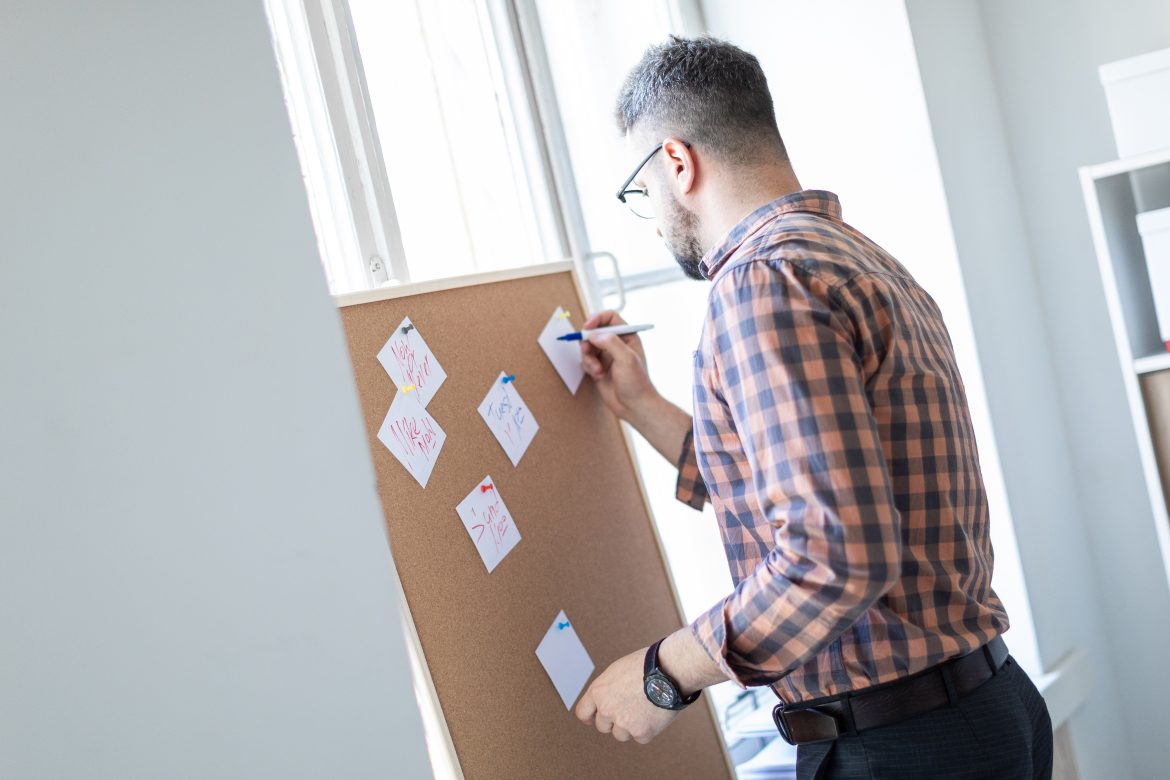 A man stands in the office near the window and writes on the stickers a marker.