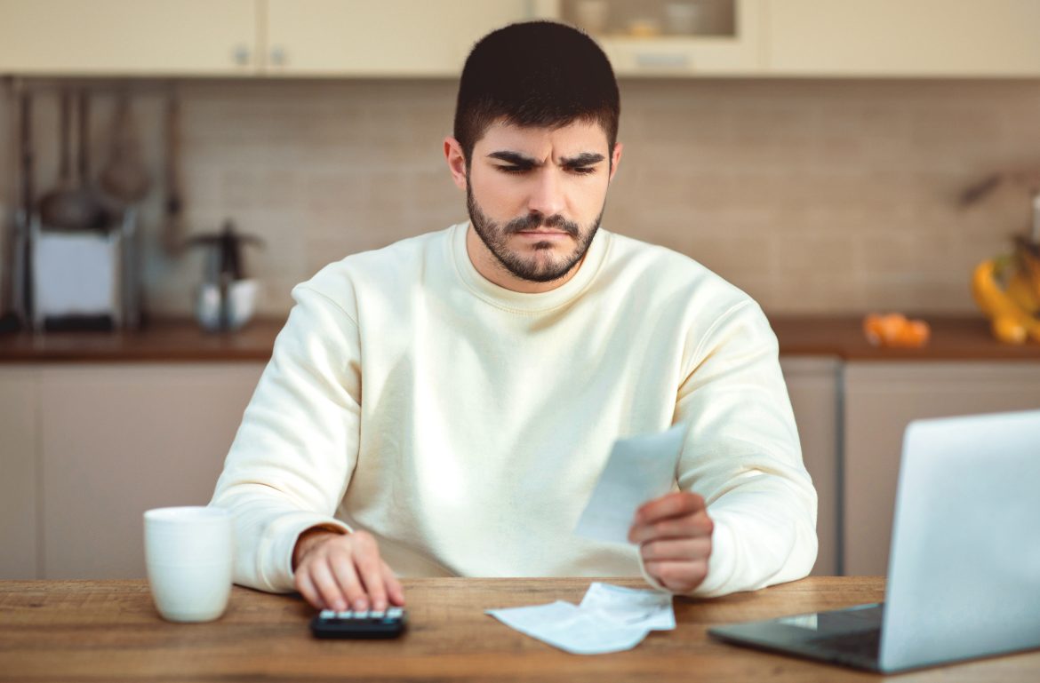 Man Sitting at Table With Calculator and Receipts